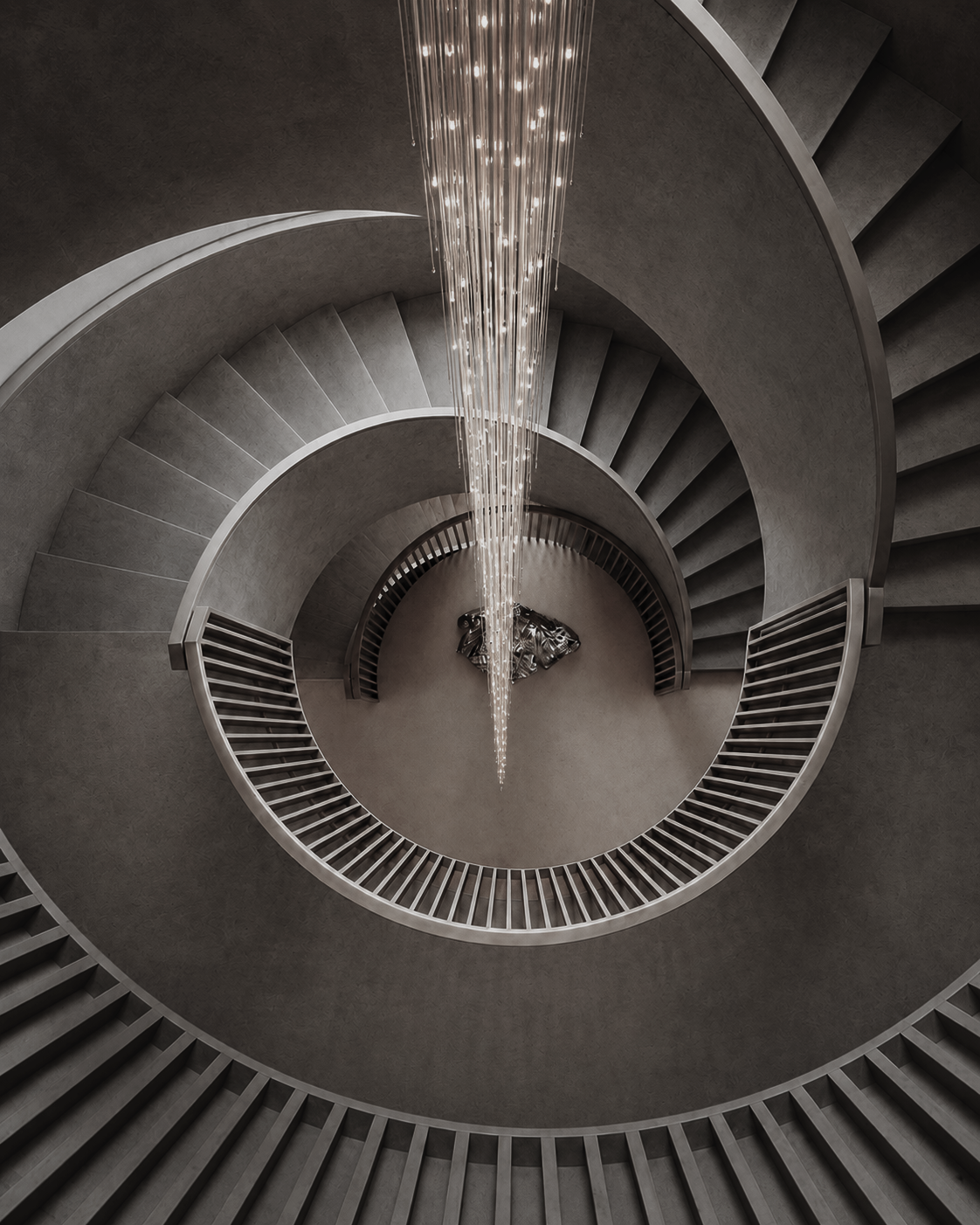 Long crystal stairwell chandelier suspended through a spiral staircase, showing vertical scale for high-ceiling entry lighting.