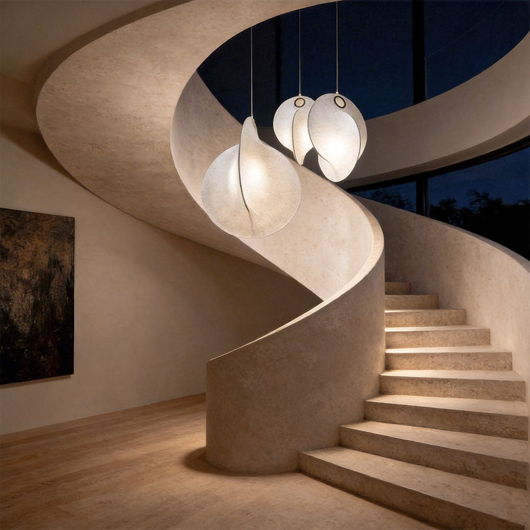 Glowing petal pendant cluster beside a curved staircase, showing vertical drop and sculptural lighting for a stairwell